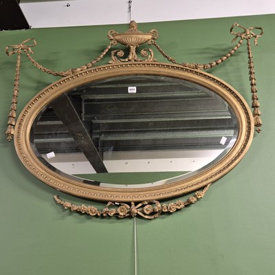 Lot 604 - A bevelled glass oval mirror in a gilt egg and...